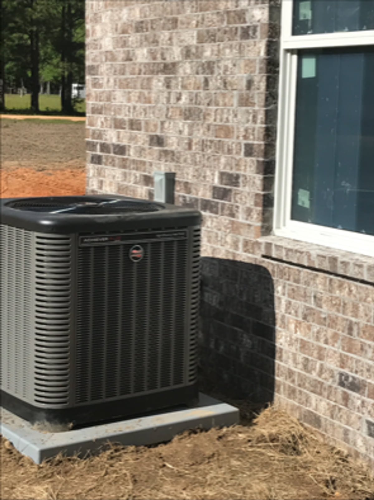 Outdoor air-conditioning condenser installed beside a brick home.