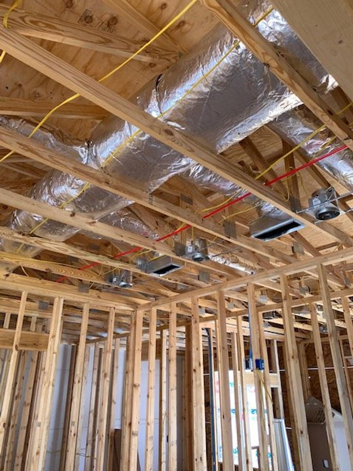 Foil-faced ductwork routed through exposed wood framing during construction.