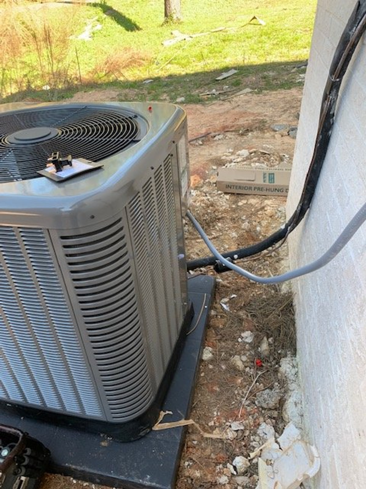 Outdoor air-conditioning condenser with refrigerant lines beside a white exterior wall.