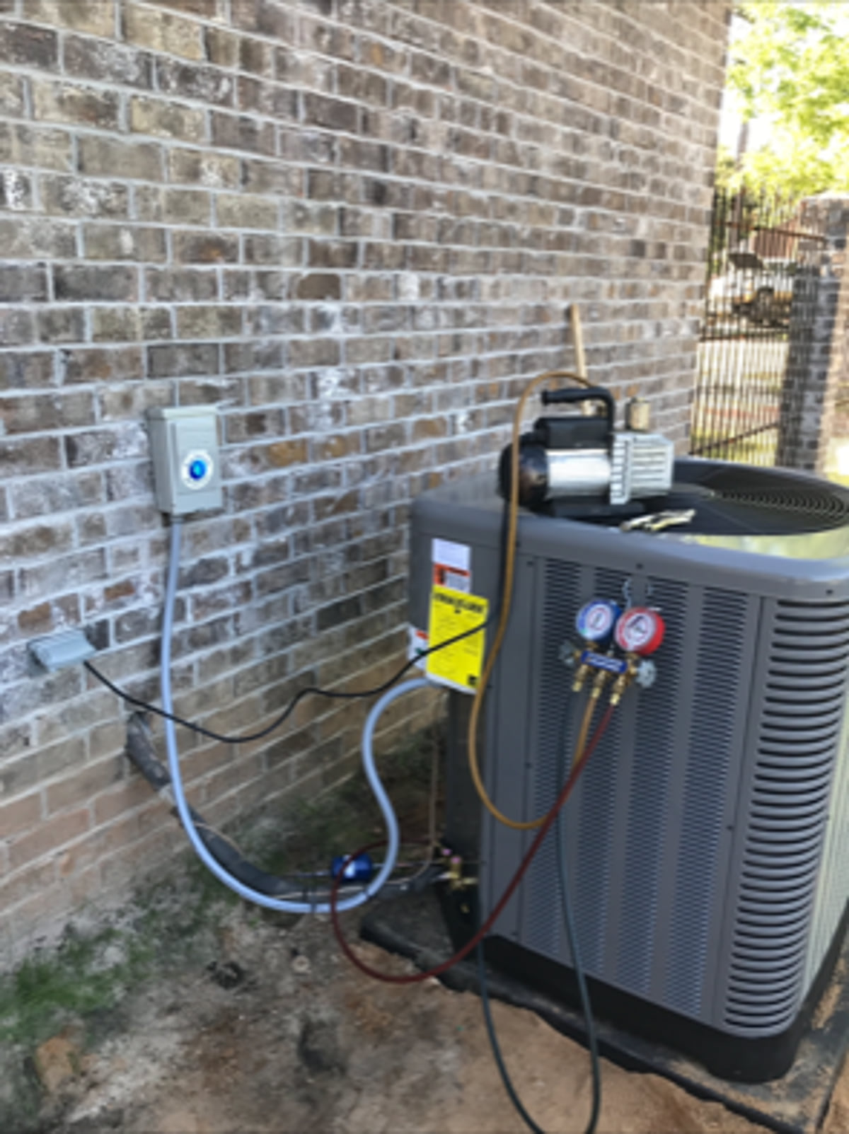 Outdoor air-conditioning condenser and service lines beside a brick wall.