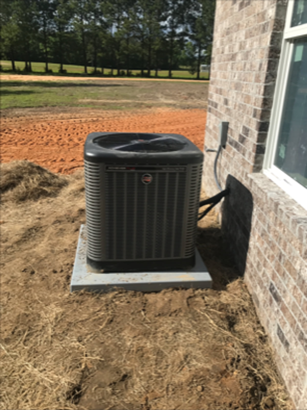 Outdoor air-conditioning condenser beside a brick home and window.