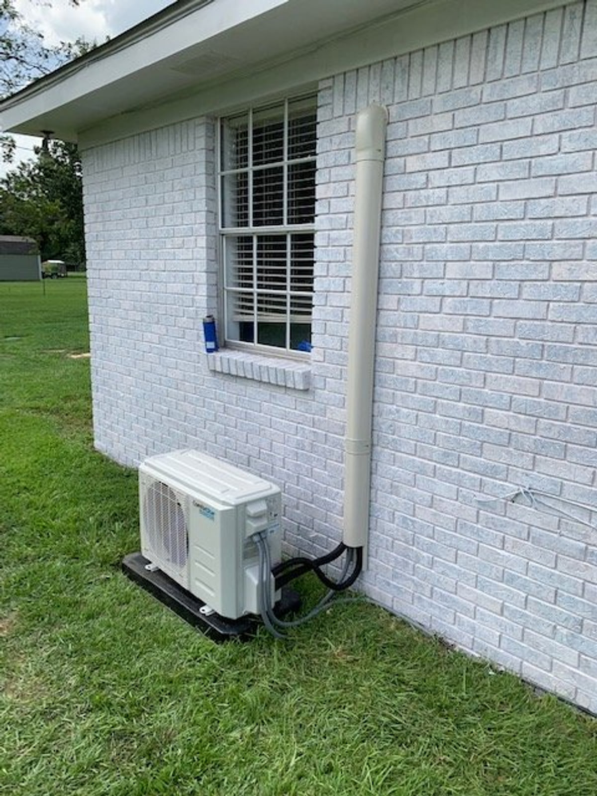 Outdoor mini-split condenser beside a white brick home.